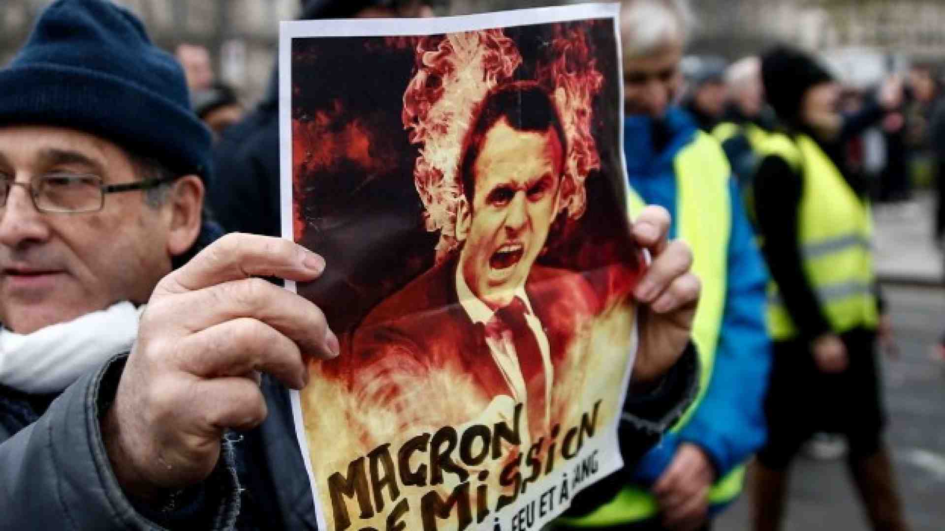 Un manifestante a Parigi espone un cartello: "Macron dimettiti" (Foto LaPresse)