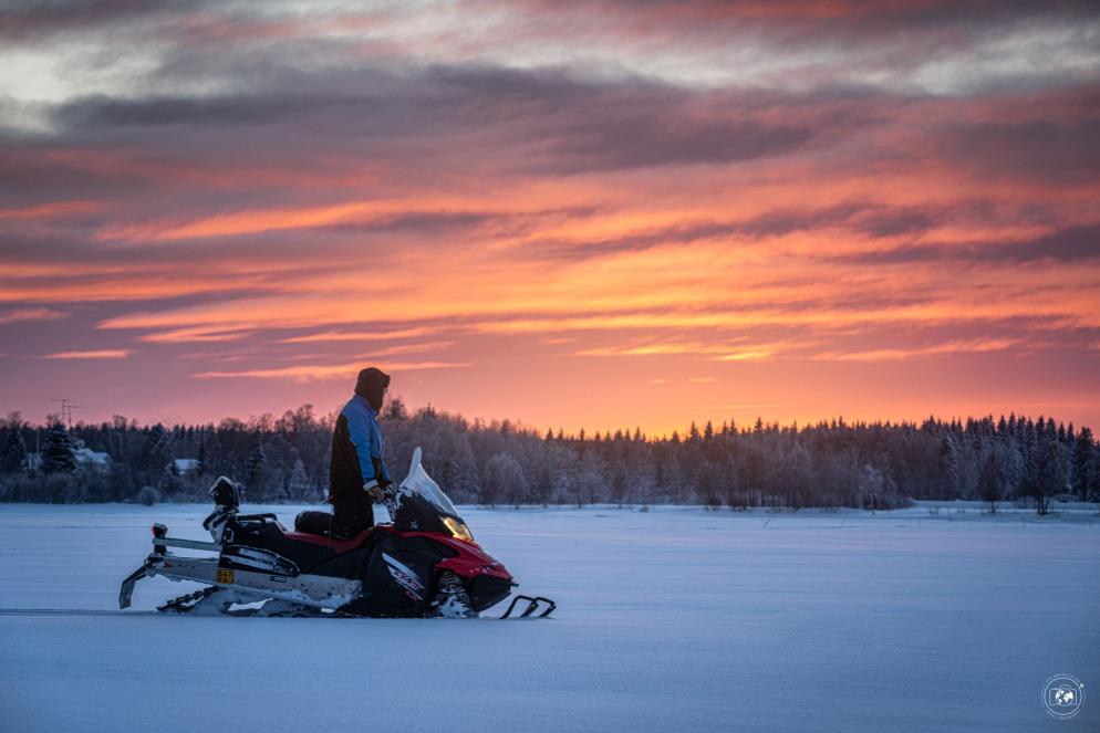 Un lappone osserva il tramonto a bordo della sua motoslitta mentre si reca a pesca
